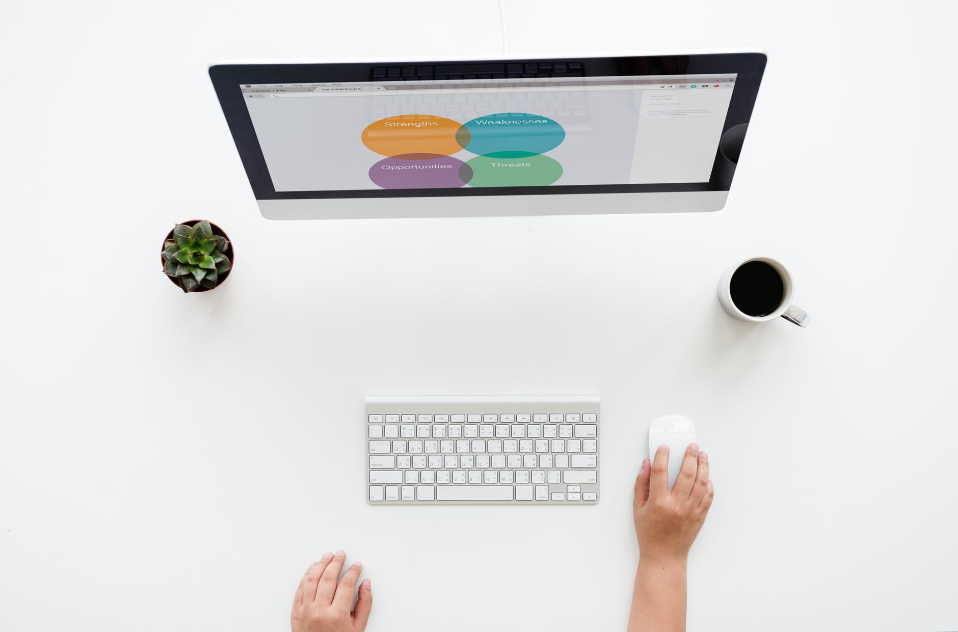 silver imac on white surface near apple keyboard and magic mouse held by human hand